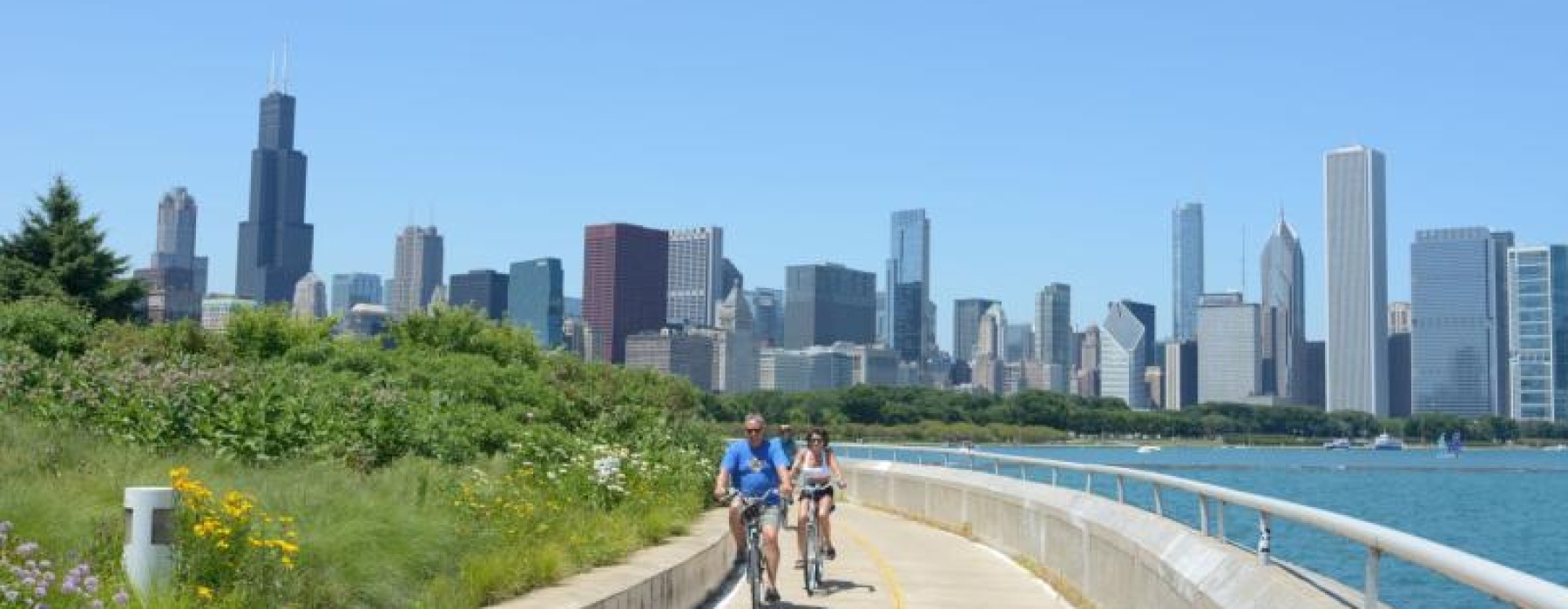 a couple riding bikes on a path with a city skyline in the background