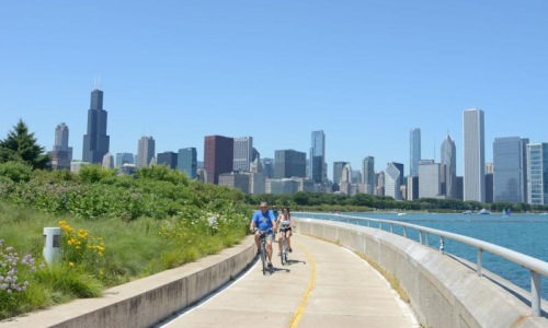 a couple riding bikes on a path with a city skyline in the background